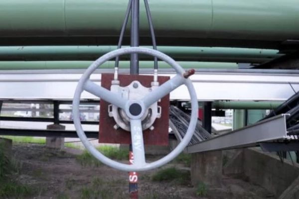 Alt text: Volantino sospeso sotto tubazioni industriali, collegato a due cavi flessibili neri.