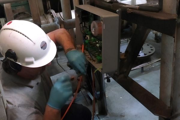Tecnico con casco al lavoro sull’elettronica di un sensore installato in impianto durante un intervento di assistenza